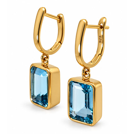 A side view of a pair of gold plated sterling silver blue topaz dangle earrings. 