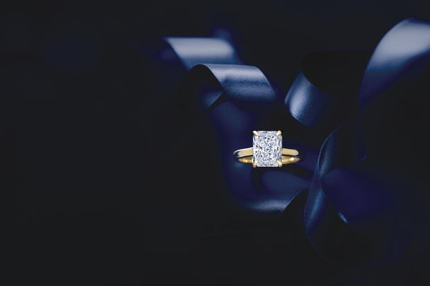 Radiant cut diamond ring held between blue fabric folds against a dark background